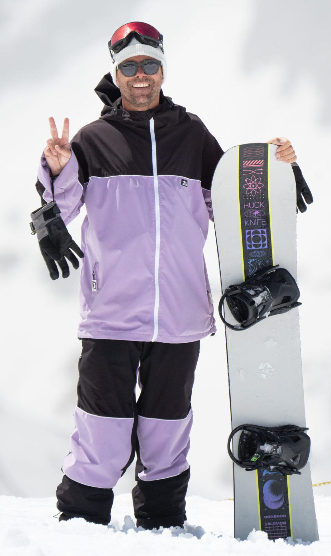 Guido, moniteur de la team de snowboard aux 2 Alpes, tenant sa planche et faisant le signe de la paix sur la neige