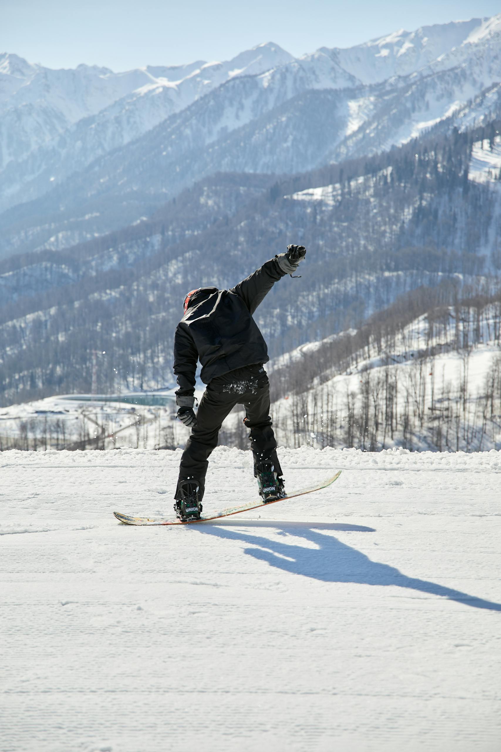 A lone snowboarder executes a thrilling move on a snow-covered mountain slope, under a clear blue winter sky.