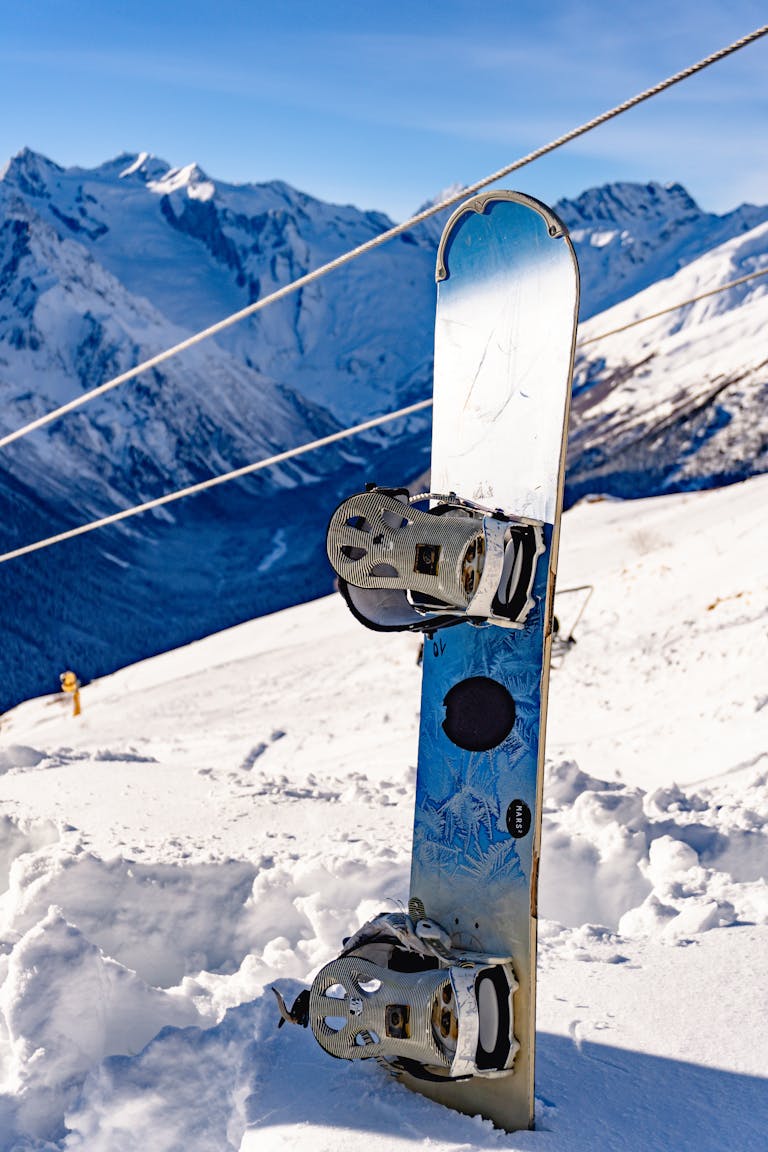 A snowboard embedded in snow against a stunning winter mountain backdrop.