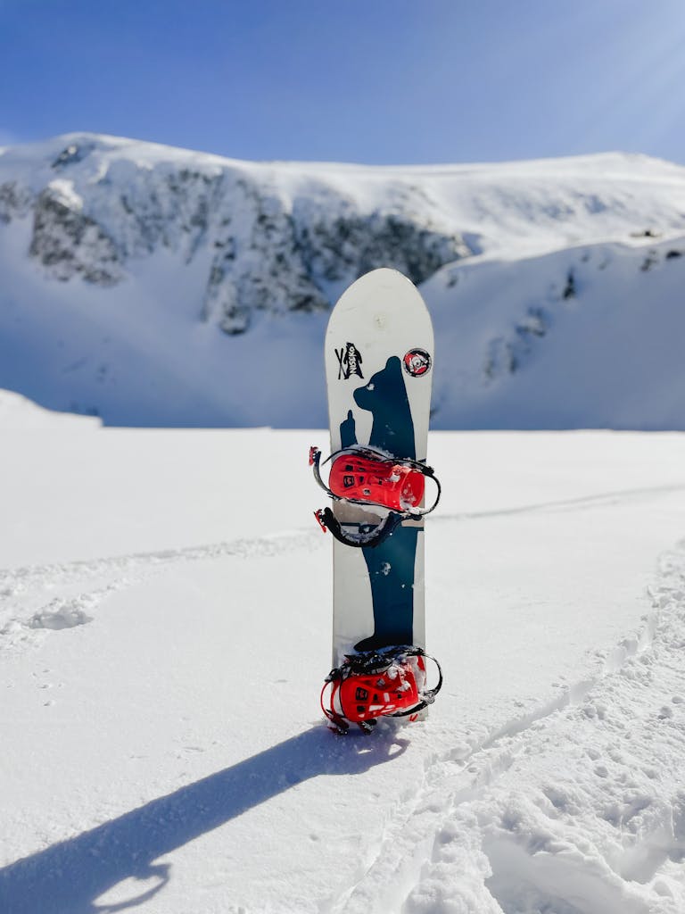 Snowboard standing upright on powdery snow with a backdrop of majestic snowy mountains.