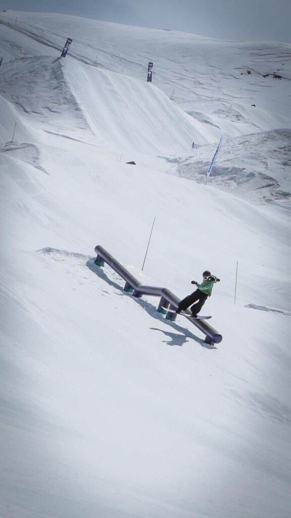 Snowboardeur en trick freestyle sur un long rail en descente dans le snowpark