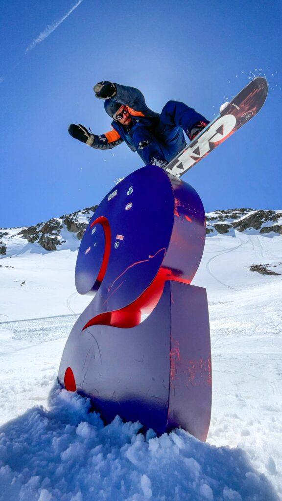Snowboarder réalisant un saut au-dessus de la sculpture “2” aux 2 Alpes durant un shooting photo