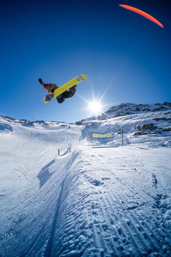 Snowboardeur effectuant un saut freestyle en plein soleil dans le snowpark des 2 Alpes