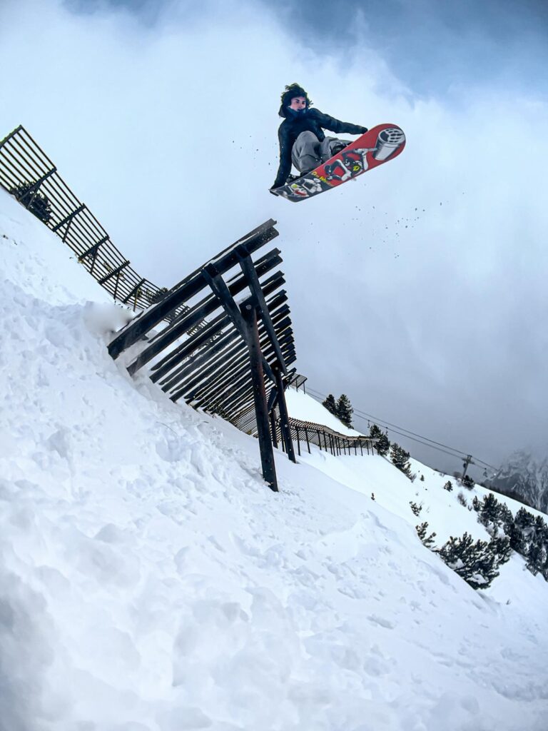 Snowboardeur réalisant un saut freestyle au-dessus d’une barrière de protection enneigée