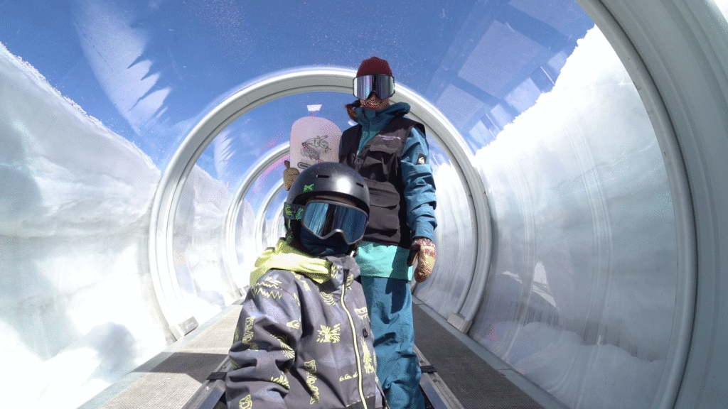 Enfants sur un tapis roulant couvert aux 2 Alpes pour rejoindre la zone d’apprentissage du snowboard