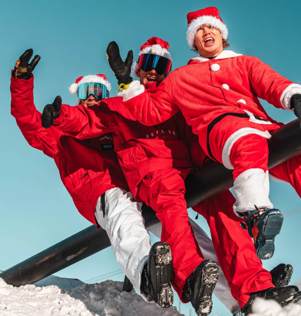 Trois snowboarders en tenue rouge et bonnet de Noël posant sur la neige aux 2 Alpes pendant un événement de snowboard